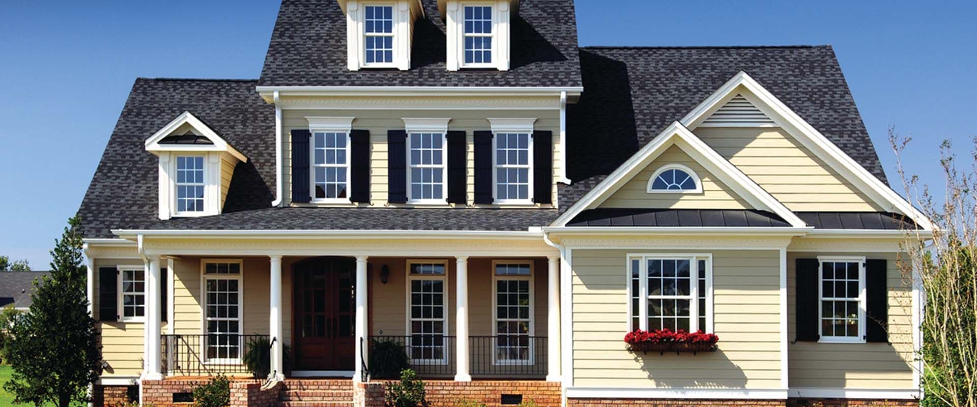 A yellow house with new siding, a porch, and black shutters.