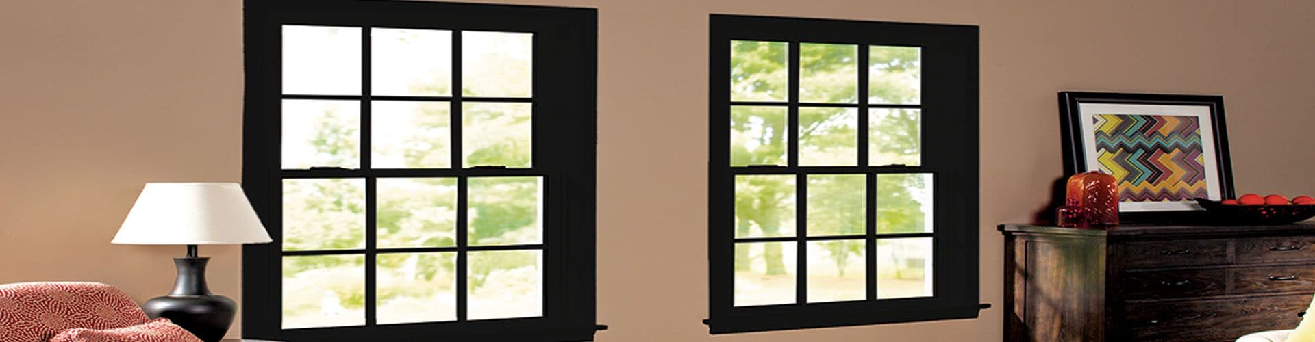Two black double-hung windows with black trim and lattices in a beige room.