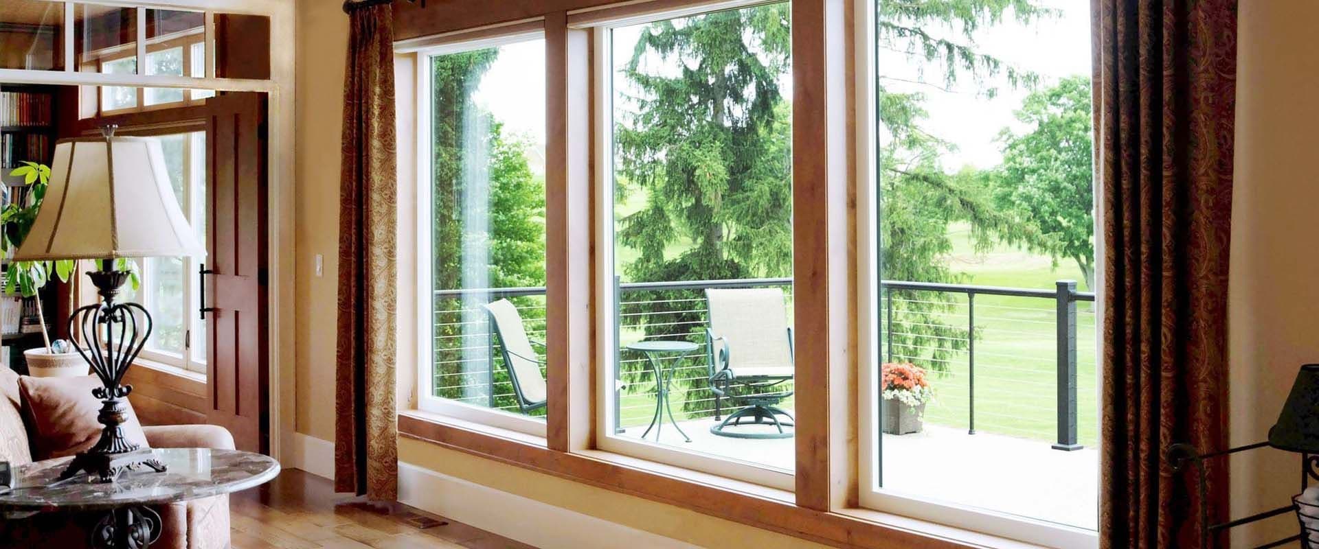 Three large picture windows look out onto a deck with patio furniture.